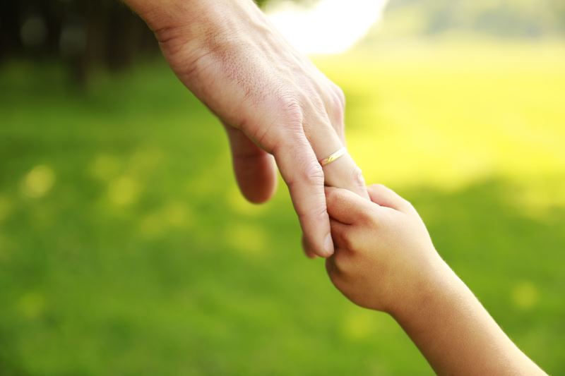 Adult holding a child's hand to guide them.